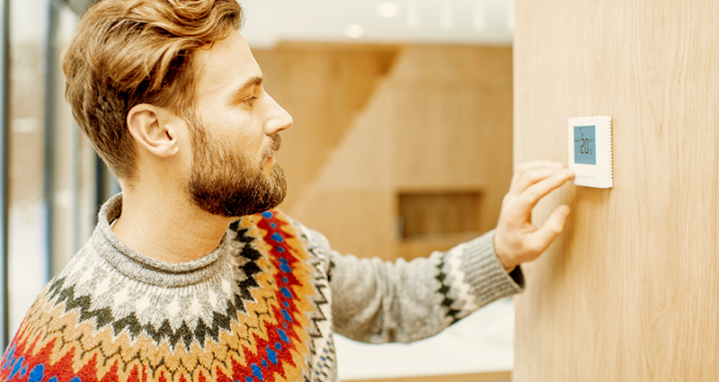 Man in sweater adjusting a digital thermostat