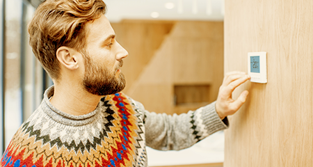 Man in sweater adjusting a digital thermostat